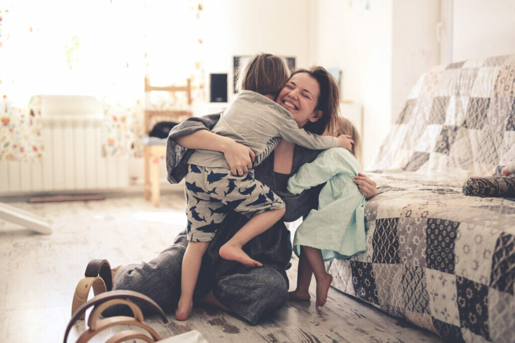 photo of a happy mom hugging her two toddler children on the floor and smiling to represent microdosing moms